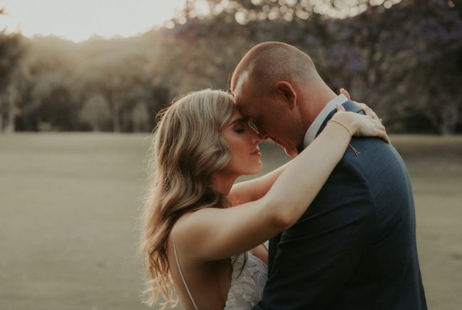 A bride and groom rest their foreheads against each other.